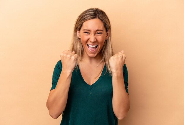 Young caucasian woman isolated on beige background cheering carefree and excited. Victory concept.