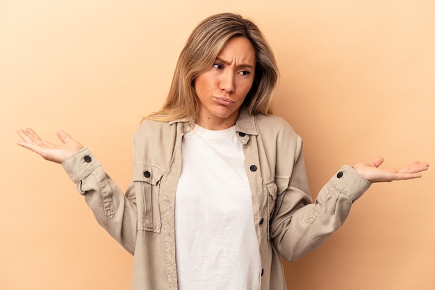 Young caucasian woman isolated on beige background confused and doubtful shrugging shoulders to hold a copy space.