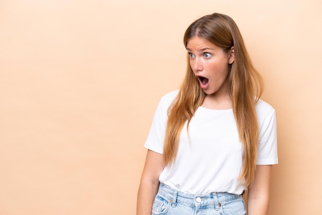 Young caucasian woman isolated on beige background doing surprise gesture while looking to the side