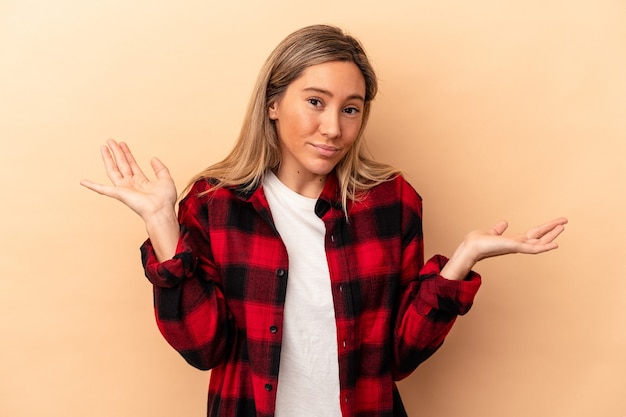 Young caucasian woman isolated on beige background doubting and shrugging shoulders in questioning gesture.