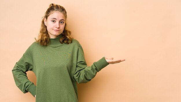 Young caucasian woman isolated on beige background doubting and shrugging shoulders in questioning gesture.