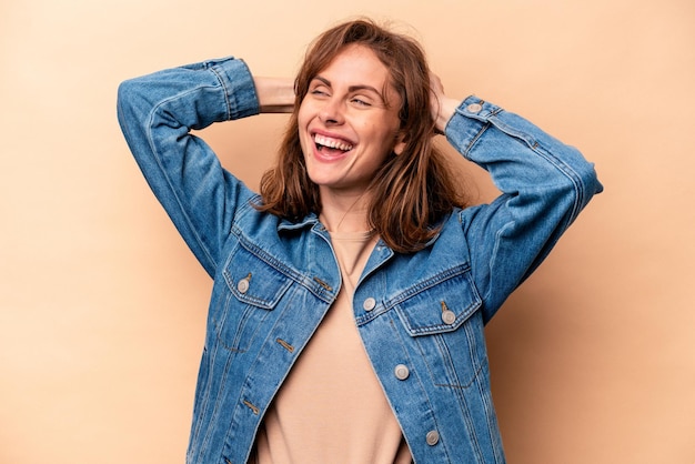 Young caucasian woman isolated on beige background feeling confident with hands behind the head