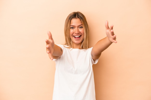 Young caucasian woman isolated on beige background feels confident giving a hug to the camera.