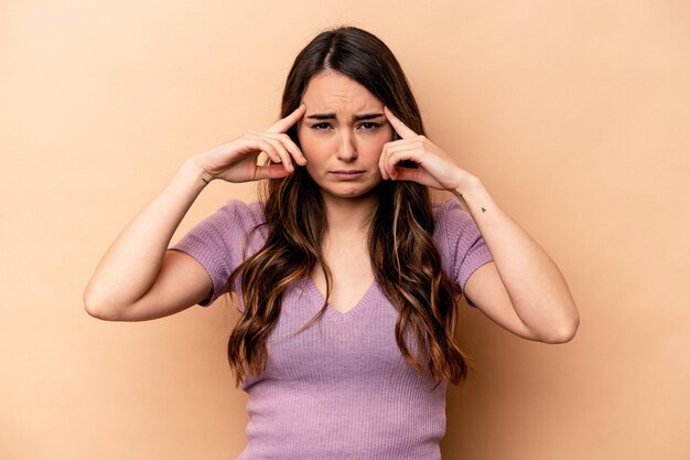 Young caucasian woman isolated on beige background focused on a task keeping forefingers pointing head