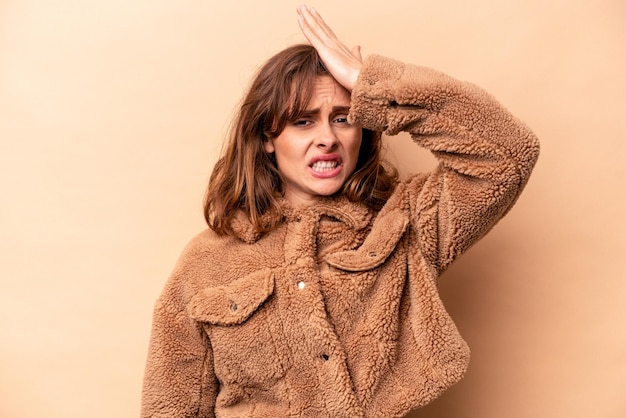 Young caucasian woman isolated on beige background forgetting something slapping forehead with palm and closing eyes
