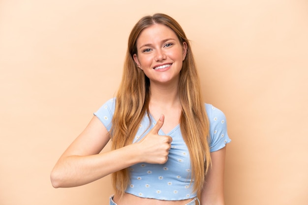Young caucasian woman isolated on beige background giving a thumbs up gesture