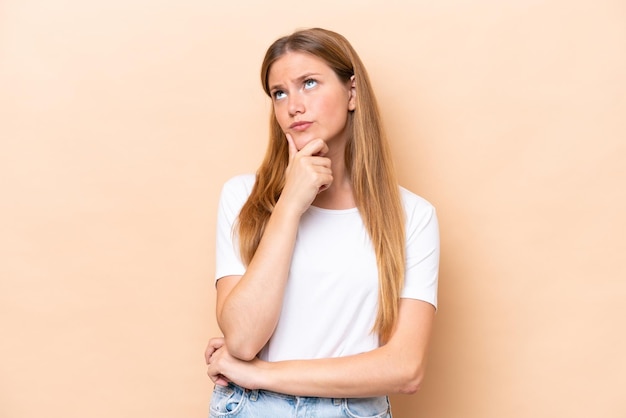 Young caucasian woman isolated on beige background having doubts