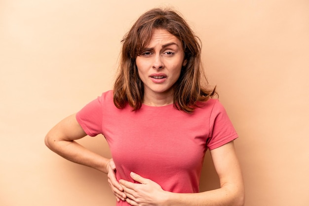 Young caucasian woman isolated on beige background having a liver pain stomach ache