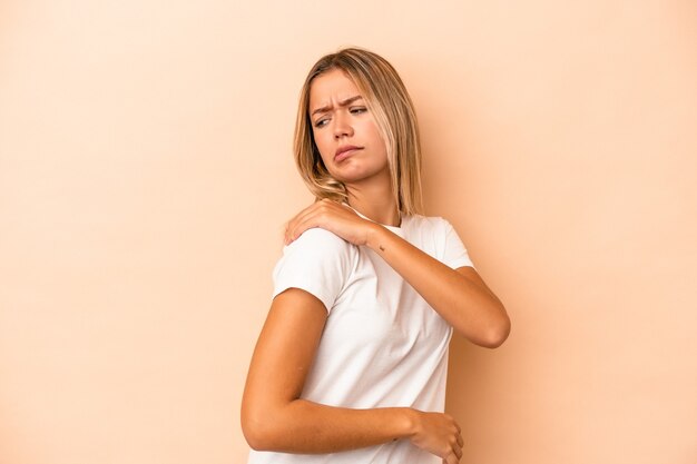 肩の痛みを持っているベージュの背景に分離された若い白人女性。