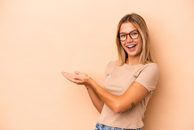 Young caucasian woman isolated on beige background holding a copy space on a palm.