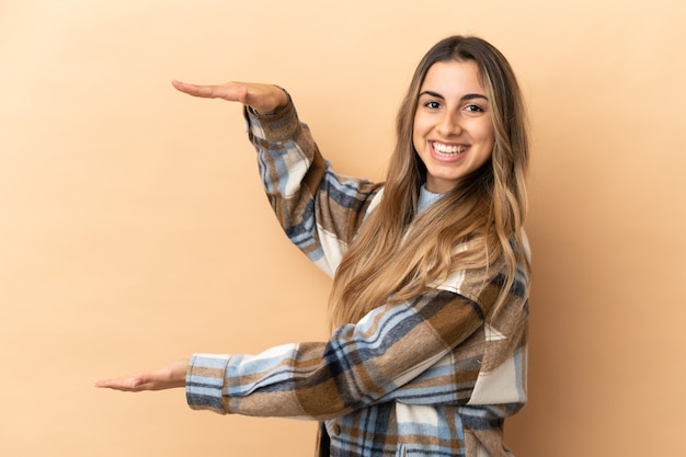 Young caucasian woman isolated on beige background holding copyspace to insert an ad