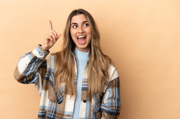 Young caucasian woman isolated on beige background intending to realizes the solution while lifting a finger up