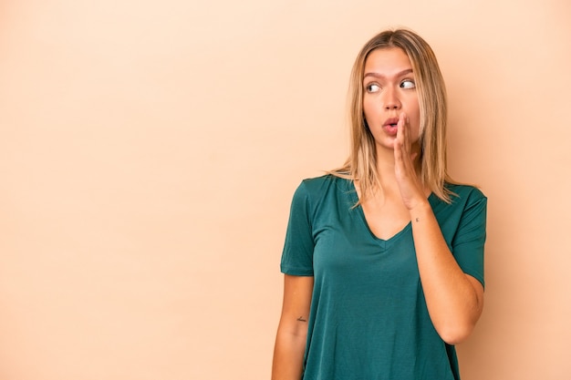 Young caucasian woman isolated on beige background is saying a secret hot braking news and looking aside