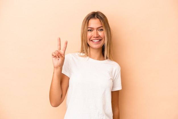 Young caucasian woman isolated on beige background joyful and carefree showing a peace symbol with fingers.