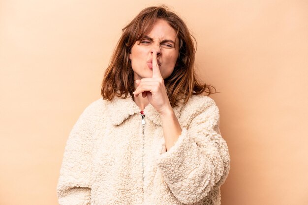 Young caucasian woman isolated on beige background keeping a secret or asking for silence