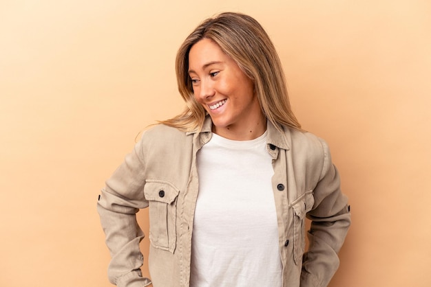 Young caucasian woman isolated on beige background laughs happily and has fun keeping hands on stomach.