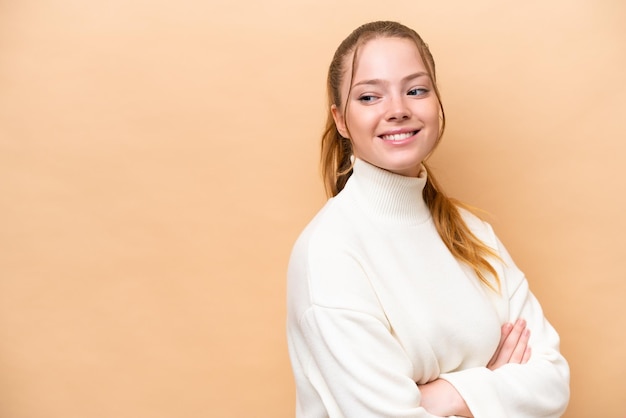 Young caucasian woman isolated on beige background looking to the side and smiling