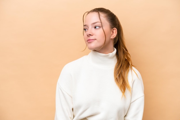 Young caucasian woman isolated on beige background looking to the side