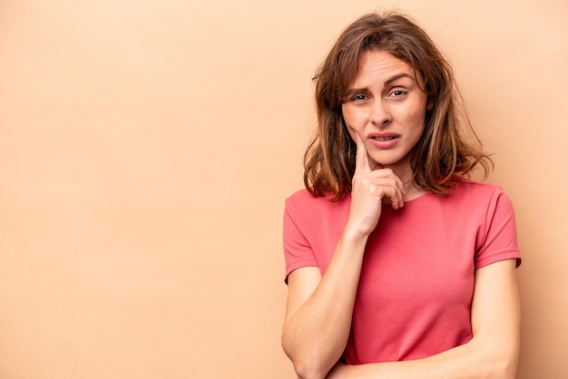 Young caucasian woman isolated on beige background looking sideways with doubtful and skeptical expression