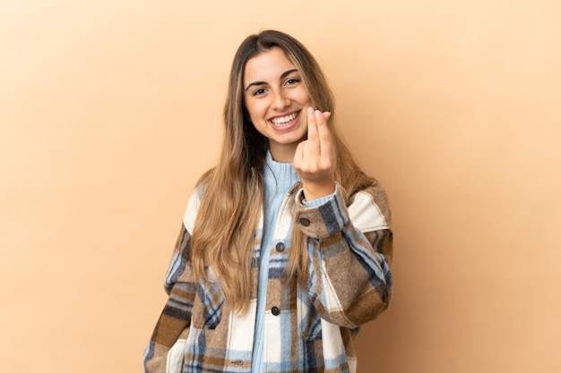 Young caucasian woman isolated on beige background making money gesture