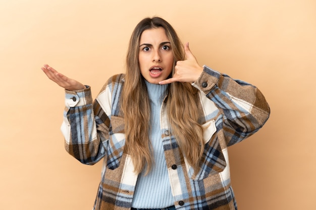 Young caucasian woman isolated on beige background making phone gesture and doubting