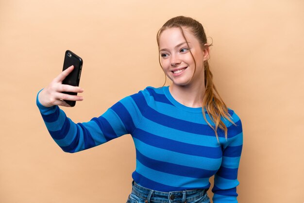 Selfie を作るベージュ色の背景に分離された若い白人女性