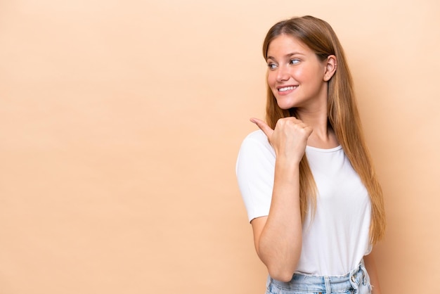 Young caucasian woman isolated on beige background pointing to the side to present a product