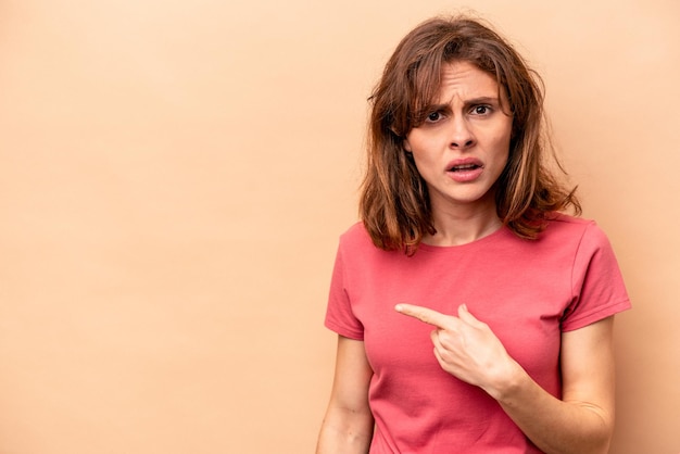 Young caucasian woman isolated on beige background pointing to the side