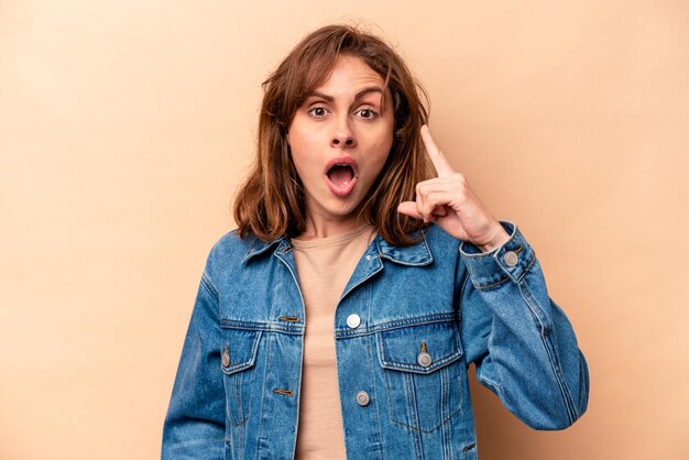 Young caucasian woman isolated on beige background pointing upside with opened mouth