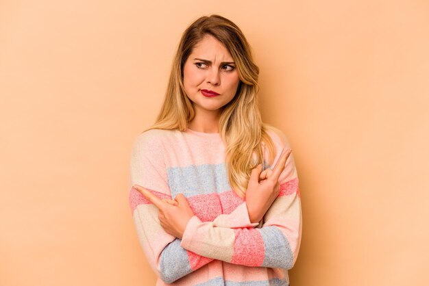 Young caucasian woman isolated on beige background points sideways is trying to choose between two options