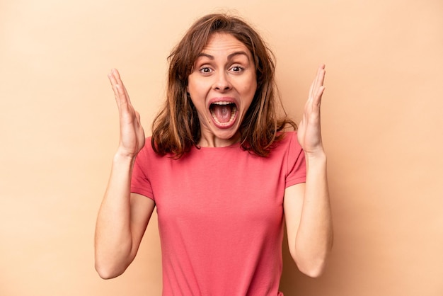 Young caucasian woman isolated on beige background receiving a pleasant surprise excited and raising hands