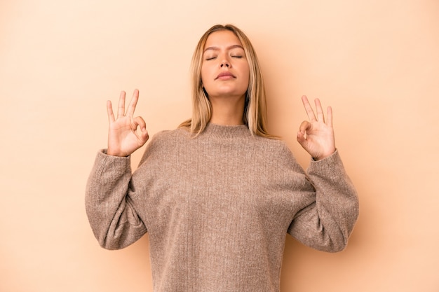 Young caucasian woman isolated on beige background relaxes after hard working day, she is performing yoga.