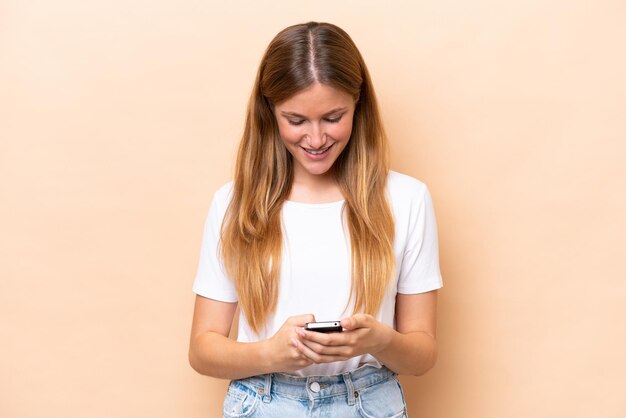 Young caucasian woman isolated on beige background sending a message with the mobile