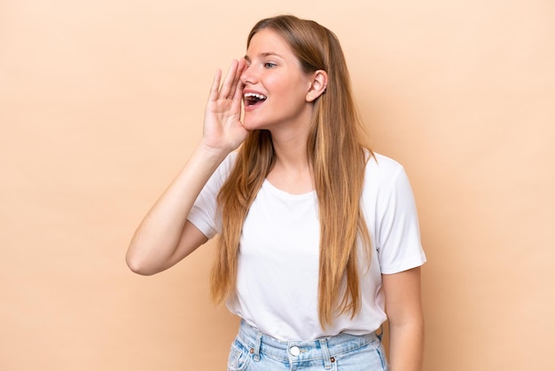 Young caucasian woman isolated on beige background shouting with mouth wide open to the side