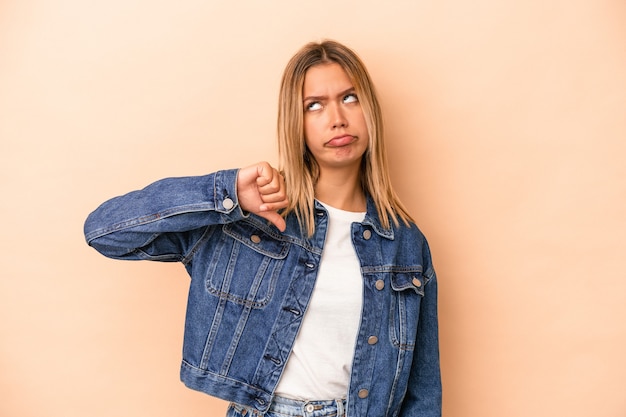 Young caucasian woman isolated on beige background showing a dislike gesture, thumbs down. Disagreement concept.