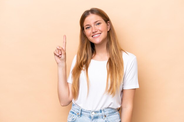 Young caucasian woman isolated on beige background showing and lifting a finger in sign of the best