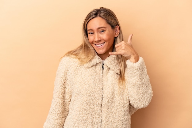 Young caucasian woman isolated on beige background showing a mobile phone call gesture with fingers.