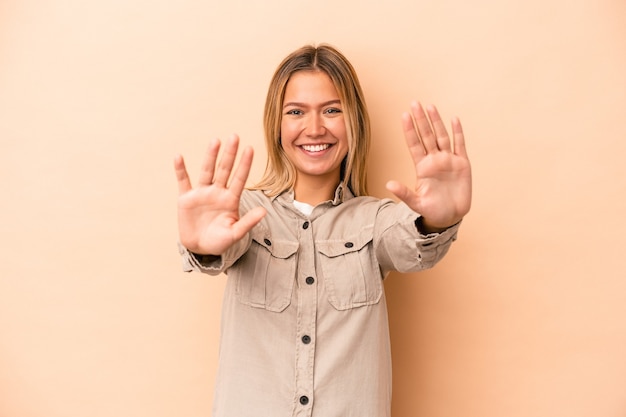 Young caucasian woman isolated on beige background showing number ten with hands.