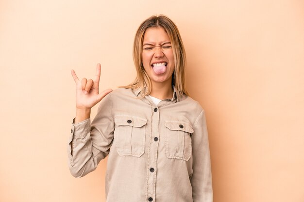 指でロックジェスチャーを示すベージュの背景に分離された若い白人女性