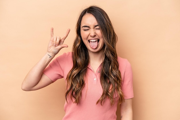 Young caucasian woman isolated on beige background showing rock gesture with fingers