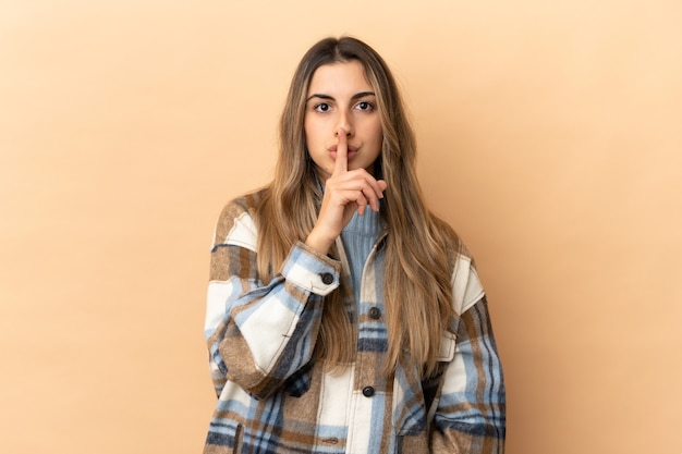 Young caucasian woman isolated on beige background showing a sign of silence gesture putting finger in mouth