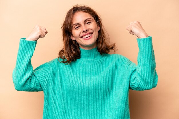 Young caucasian woman isolated on beige background showing strength gesture with arms symbol of feminine power