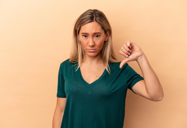 Young caucasian woman isolated on beige background showing thumb down, disappointment concept.