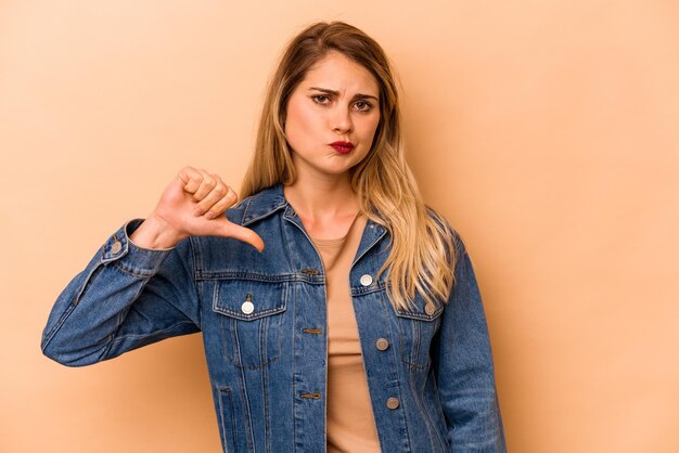 Young caucasian woman isolated on beige background showing thumb down disappointment concept