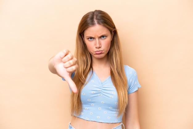 Young caucasian woman isolated on beige background showing thumb down with negative expression
