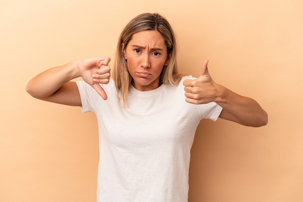 Young caucasian woman isolated on beige background showing thumbs up and thumbs down, difficult choose concept