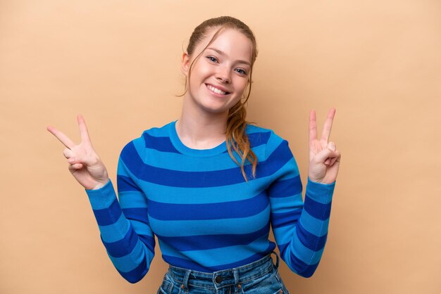 Young caucasian woman isolated on beige background showing victory sign with both hands
