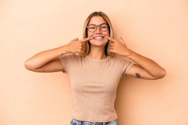 Young caucasian woman isolated on beige background smiles, pointing fingers at mouth.