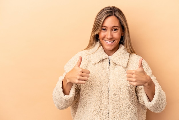 Young caucasian woman isolated on beige background smiling and raising thumb up