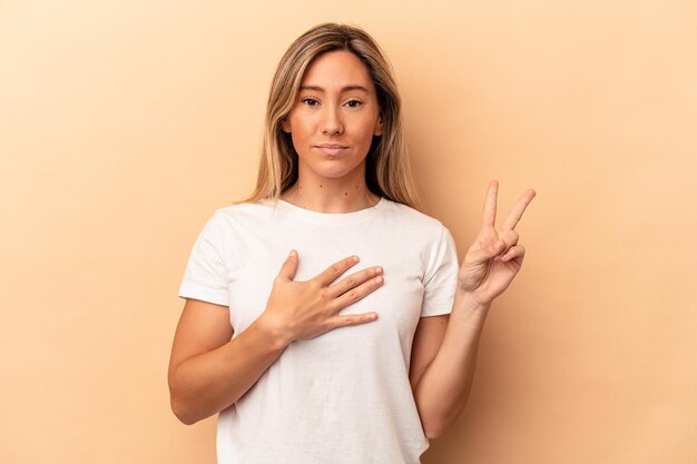 Young caucasian woman isolated on beige background taking an oath, putting hand on chest.